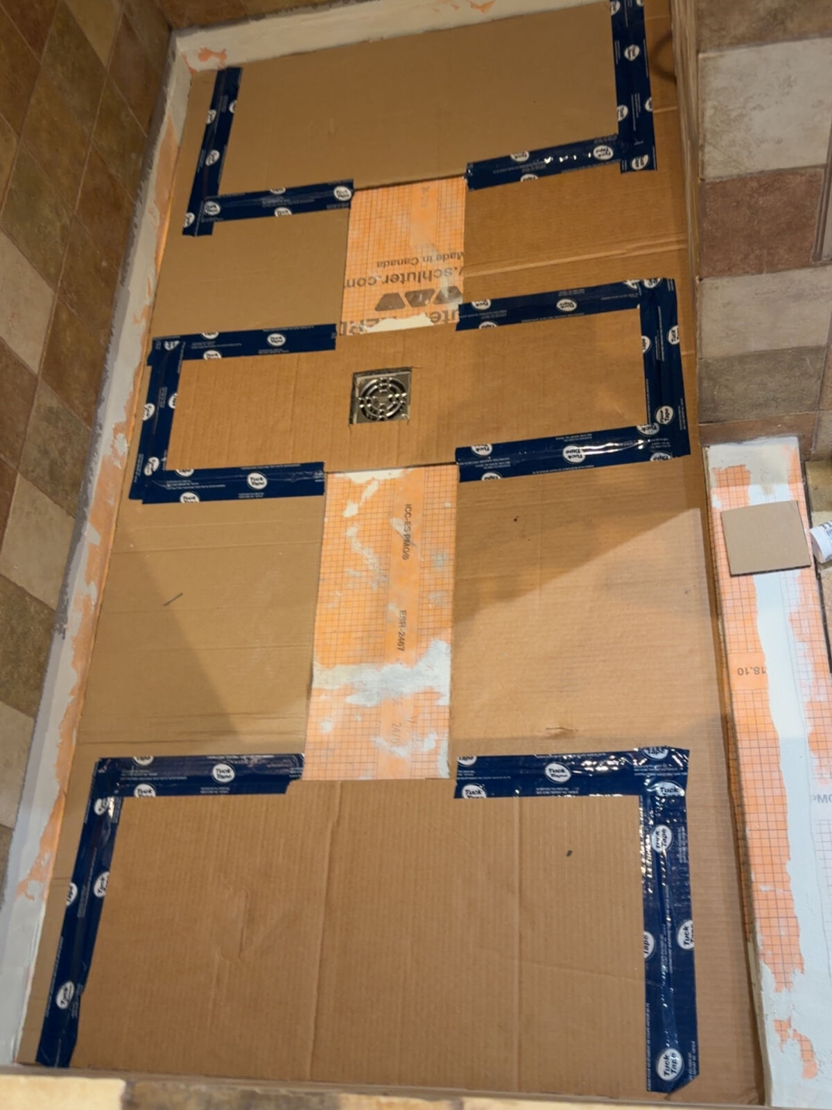 Membrane d'étanchéité orange posée sur le fond de douche, gabarits de carton pour les coupes