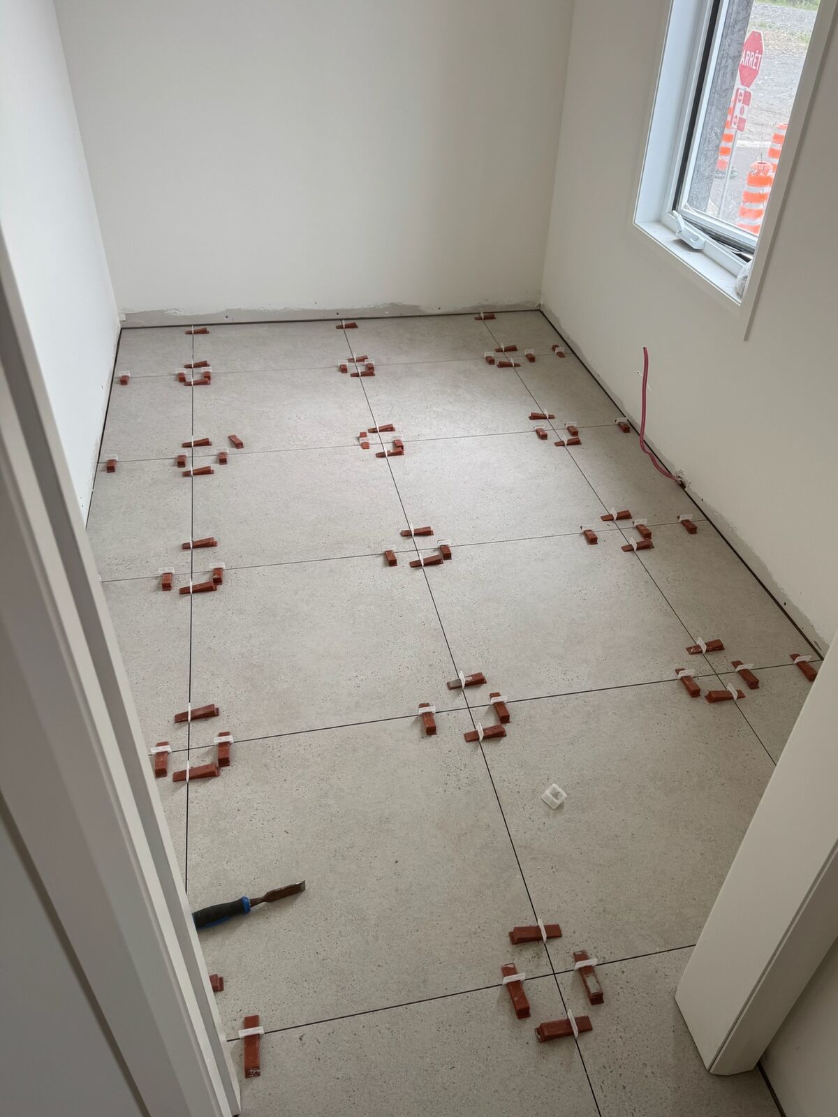 Plancher grand format gris en cours de pose dans un vestibule, avec système de nivellement